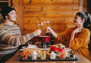 Couple toasting with white wine over a cheese fondue in the wood-panelled Adlerstube, with bread, potatoes, gherkins, pickled onions and cherry tomatoes on the table