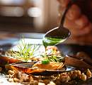 Chef versant une sauce verte sur un plat finement dressé avec des moules et des herbes fraîches – une cuisine durable au Sunstar Hotel.