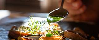 Chef versant une sauce verte sur un plat finement dressé avec des moules et des herbes fraîches – une cuisine durable au Sunstar Hotel.
