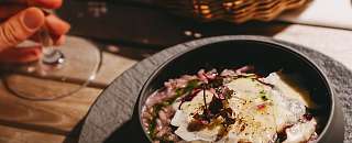 Risotto finement présenté dans un bol noir, servi avec du pain et un verre de vin blanc – une cuisine régionale et durable au Sunstar Hotel.